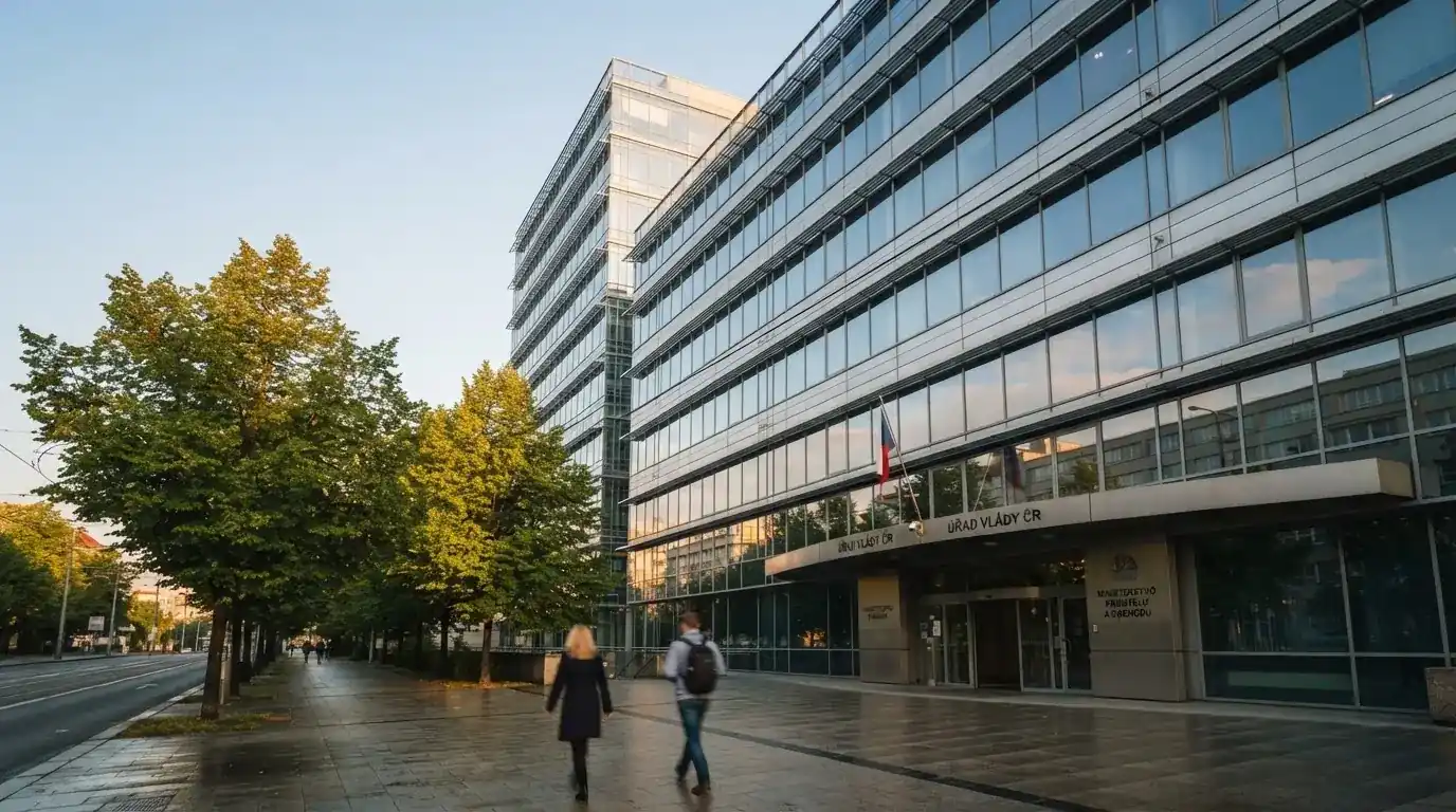 Fasáda moderní administrativní budovy s skleněnými okny odráží ranní oblohu nad rušnou pražskou ulicí.